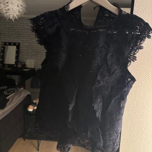 Spetsblus  - Säljer en elegant marinblå spetsblus från Zara. Blusen har ett vackert blommönster och är ärmlös, vilket gör den perfekt för både vardag och fest. Den är tillverkad i ett fint spetsmaterial som ger en lyxig känsla. Storlek xs 