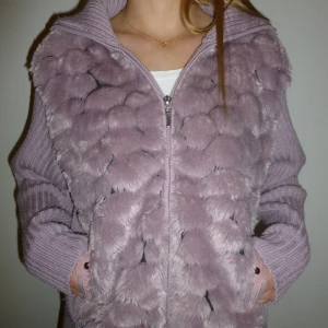 Lila pälskofta med dragkedja - Denna mysiga lila kofta med dragkedja och stickade detaljer säljer vi till ett super nice pris. Fluffig framsida och en ribbad baksida, perfekt för kyliga sommarkvällar eller varmare höstdagar💜