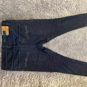 Blåa jeans från Nudie  - Blåa Nudie jeans som har ett undvik grönt märke på bak fickan
