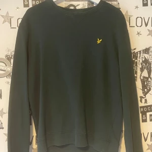 Grön tröja från Lyle & Scott - Säljer en stilren grön tröja från Lyle & Scott med deras ikoniska gula logga på bröstet. Tröjan har långa ärmar och en rund halsringning. Perfekt för en avslappnad stil. 🟢