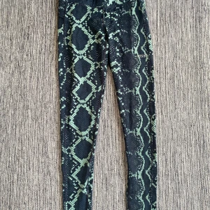 Mönstrade leggings från Casall - Snygga leggings från Casall med ett coolt ormmönster i grönt och svart. Perfekta för träning eller en avslappnad dag. De har en tight passform och är tillverkade i ett stretchigt material för bästa komfort. Gröna ormskinnsmönstrade träningstights strl S från Casall.  Byxorna har en ficka i ena sidan.  Sparsamt använda och i fint begagnat skick.  Mått Midjan: ca 34 cm Längd från grenen och ner: ca 74 cm  Polyester och elastan  Kommer från ett djur och rökfritt hem.