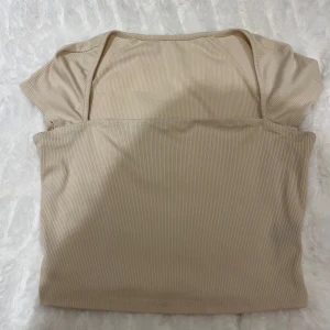 Beige ribbad topp - Säljer en stilren beige ribbad topp med korta ärmar. Perfekt för en avslappnad look. Toppen har en enkel design och är gjord i ett mjukt material.