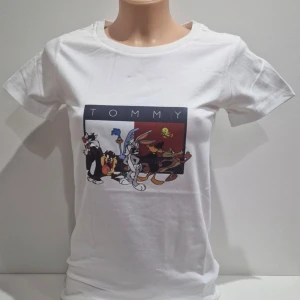 Vit T-shirt med Looney Tunes från Tommy Jeans - Säljer en vit T-shirt från Tommy Jeans med ett coolt Looney Tunes-tryck på framsidan. T-shirten har korta ärmar och är gjord i mjuk bomull. Perfekt för dig som älskar klassiska tecknade karaktärer!
