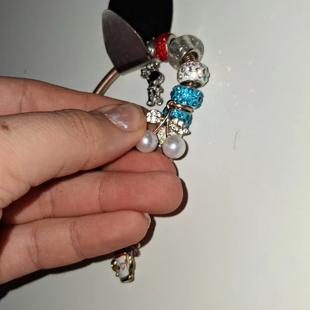 Charmigt armband med flera färgglada pärlor och berlocker, inklusive körsbär och en julkopp. Pärlorna är i olika färger som blå, rosa och silver, och vissa är glittriga. Perfekt för att ge en personlig touch till din stil.. Asusteet.