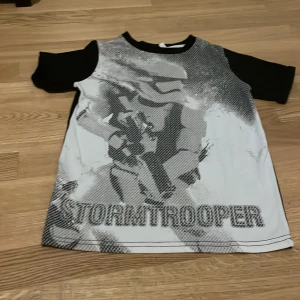Svart och vit Stormtrooper t-shirt - Cool t-shirt med Stormtrooper-tryck i svart och vitt. Den har korta ärmar och en kontrasterande design med svart baksida och ärmar. Perfekt för alla Star Wars-fans!