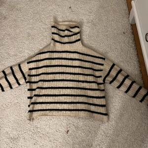 Beige och svart randig polotröja från H&M - Säljer en mysig beige polo tröja från H&M med svarta ränder. Tröjan är ribbad och har långa ärmar, perfekt för kyligare dagar. Den har en avslappnad passform och är superbekväm att bära. Hör av dig vid intresse! 🖤