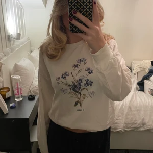 Vit långärmad tröja med blommotiv - Säljer en vit långärmad tröja med blommotiv i lila och grönt på framsidan. 