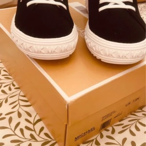 Svarta sneakers från Michael Kors - Snygga svarta sneakers från Michael Kors med vita snören och sula. Perfekta för en stilren look. Märkeslogga synlig på sidan och sulan.