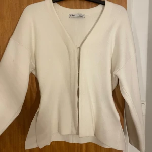 Vit kofta från Zara - Säljer en stilren vit kofta från Zara med v-ringning och knäppen framtill. Koftan har långa ärmar och en mjuk, bekväm passform. Perfekt för lager-på-lager under kyligare dagar.