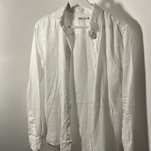Vit linneskjorta från Zara - Säljer en stilren vit skjorta från Zara i linne. Skjortan har långa ärmar och knappar framtill. Perfekt för en avslappnad men ändå elegant look. Skjortan är endast använd ett par gånger, så inga defekter alls. Skjortan är i storlek S.