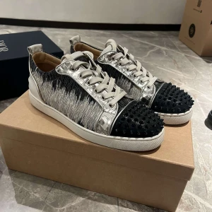 LOUBITINS - Unika sneakers med en kombination av silver och svart. Skorna har en iögonfallande design med svarta nitar på tån och ett mönster som liknar penseldrag. De har snörning och en röd sula som ger en modern touch. Kvitto och allt og medföljer!