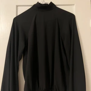 Svart långärmad polotröja - Snygg svart polotröja med långa ärmar. Perfekt för en stilren look. Tröjan har en hög krage och är tillverkad i ett mjukt material som ger en bekväm passform.