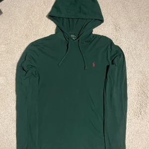 Ralph Lauren - Säljer en snygg grön hoodie från Ralph Lauren med en liten röd logga på bröstet. Perfekt för en avslappnad stil.
