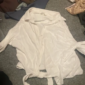Vit blus från H&M - Säljer en stilren vit blus från H&M i storlek 42. Blusen har en knytning framtill och är tillverkad i ett lätt och luftigt material. Perfekt för en avslappnad look. 💫
