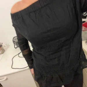 Svart offshoulder topp - Snygg svart offshoulder topp med långa ärmar och spetsdetaljer. Perfekt för en stilren look med en touch av elegans. Toppen har en åtsittande passform och är tillverkad i ett bekvämt material.