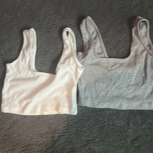 Vita och gråa ribbade linnetoppar från Even&Odd - Säljer två ribbade linnetoppar från Even&Odd i vitt och grått. De är ärmlösa och har en enkel design som passar perfekt till vardags. Topparna är croppade och gjorda i ett mjukt material.