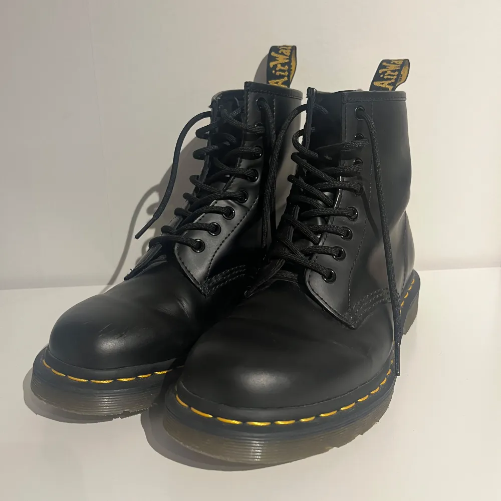 Säljer ett par klassiska svarta Dr. Martens boots i skinn med den ikoniska gula sömmen. De har snörning och en robust sula som är perfekt för höst och vinter. Kängorna har endast använts enstaka gånger, men har en liten defekt fram på skon (visat på bilden). Hund finns i huset.. Skor.