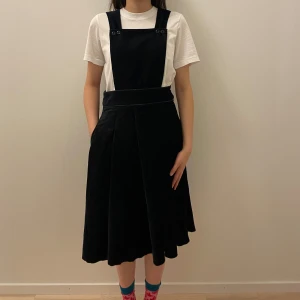 Svart klänning med hängslen från Initial - Säljer en svart klänning med hängslen från Initial. Klänningen har en stilren design med en A-linjeformad kjol och knappar vid hängslena. Perfekt för både vardag och festliga tillfällen. Materialet känns mjukt och bekvämt. Passar bra med en t-shirt under för en avslappnad look.