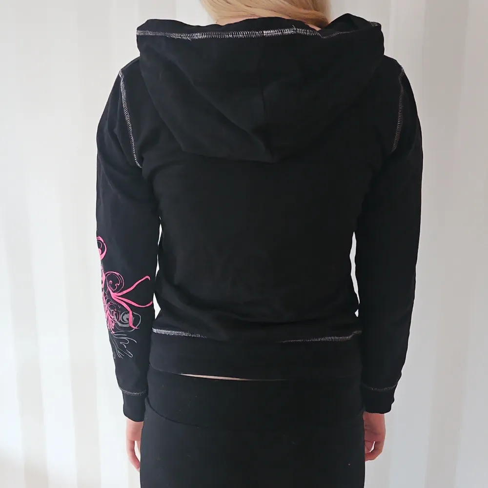 Säljer en cool svart hoodie med färgglatt blommigt mönster i rosa och gult. Den har en dragkedja framtill och luva. Perfekt för en avslappnad stil med lite edge. Är i barnstorlek men motsvarar en 34.. Tröjor & Koftor.