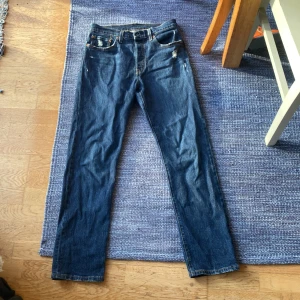 Blå jeansbyxor - Säljer ett par klassiska blå jeans från Levis i bra skick. De har en straight passform och är midwaist. Byxorna har snygga slitningar och en dragkedja. Perfekta för både vardag och fest! Använda fåtal gånger. Självklart är priset diskuterbart vid snabb affär. Sitter som 29:32