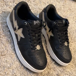 Svarta sneakers från Bape - Säljer ett par svarta Bape sneakers i mycket bra skick. De har en cool stjärndetalj på sidan och klassisk snörning. Perfekta för både vardag och fest! Storlek 41 köpta för 4500 dem har en skada hos solurna som jag fixade man kan knappast se den.