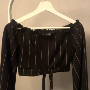 Svart offshoulder topp med vita ränder - Snygg svart offshoulder topp med vita ränder. Den har långa ärmar och en söt knytning framtill. Perfekt för både vardag och fest! 🖤