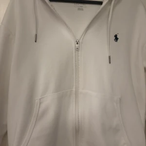 Vit hoodie från Polo Ralph Lauren - Säljer en stilren vit hoodie från Polo Ralph Lauren i bra skick. Den har en dragkedja framtill och en klassisk logga på bröstet. Perfekt för både vardag och chill dagar. Storleken är normal och materialet är mjukt och bekvämt. Inga skador och helt ny 10/10 skick. Säljer pga storleken är lite för stor. Ställ gärna frågor! ”Pris kan diskuteras!”
