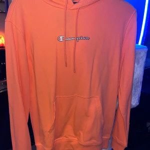 Orange hoodie från Champion - Säljer en snygg orange hoodie från Champion i bra skick. Den har en klassisk passform med långa ärmar och en känguruficka framtill. Perfekt för höst och vår, eller när du bara vill chilla hemma. 🧡