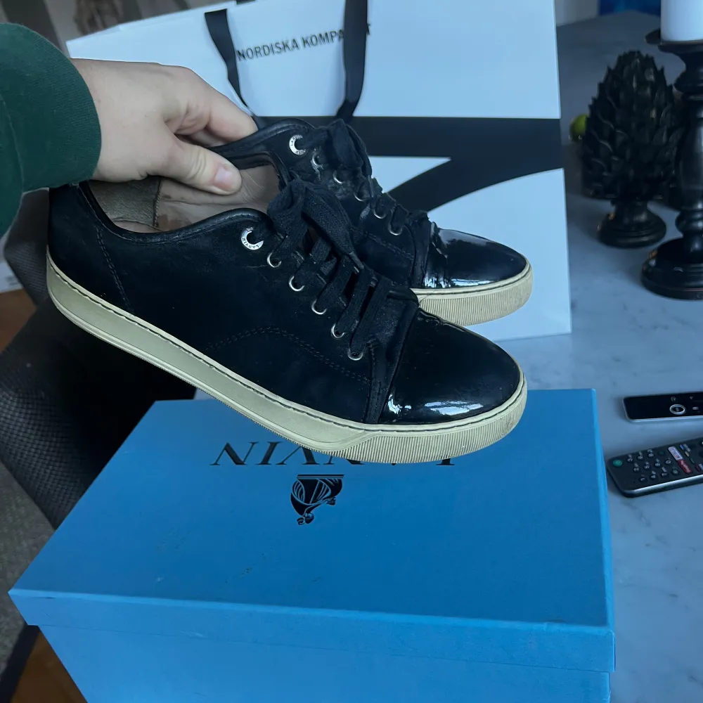 Säljer ett par snygga svarta Lanvin sneakers med glansiga lackdetaljer på tån och hälen. Skorna har en vit sula och klassisk snörning. Perfekta för både vardag och fest! De är i bra skick och redo för nya äventyr.. Kengät.