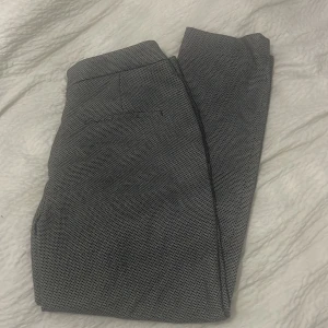 Grå mönstrade byxor från H&M - Säljer ett par grå mönstrade byxor från H&M i storlek 40. De har en elegant och stilren look, perfekt för både vardag och fest. Byxorna är i bra skick och har en normal passform. Materialet känns bekvämt och är lätt att matcha med olika toppar.