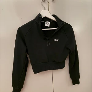 Svart croppad hoodie från ICANIWILL - Säljer en snygg svart croppad hoodie från ICANIWILL. Den har en halv dragkedja framtill och är perfekt för både träning och vardag. Materialet är mjukt och bekvämt, och den har långa ärmar med ribbade muddar. Perfekt för en sportig look! 🖤