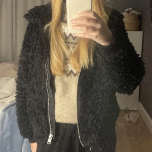 teddyjacka med dragkedja - Mysig svart teddyjacka med dragkedja framtill. Perfekt för höst och vinter med sin fluffiga och varma design. Jackan har långa ärmar och en bekväm passform. Perfekt för att hålla sig varm och stilren under kyliga dagar. (1 bilden är lånad)