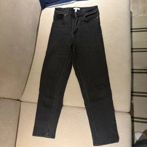 Svarta jeans med blommigt broderi - Säljer ett par svarta jeans från H&M i storlek S. De är högmidjade och har en straight passform. På bakfickan finns ett fint blommigt broderi i olika färger. Perfekta för både vardag och fest! 🌸