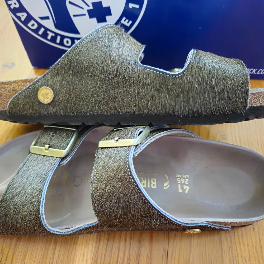 These Birkenstock Arizona Rivet Logo sandals are in the color Olive Melange. They are in perfect condition. Size: 41, narrow fit. Real fur on top.. Skor.