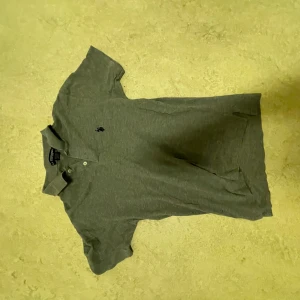 Grå pikétröja från U.S. Polo Assn. - Säljer en stilren grå pikétröja från U.S. Polo Assn. i storlek L. Tröjan har korta ärmar och en klassisk krage med två knappar. Perfekt för både vardag och lite finare tillfällen. Den är i bra skick och redo för en ny ägare!