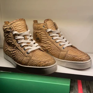 Christian Louboutin - Snygga beige sneakers från Christian Louboutin med ett coolt ormskinnsmönster. De har vita snören och den ikoniska röda sulan. Perfekta för att ge din outfit en lyxig touch. Skorna är i mycket bra skick och är i sktolek 39 1/2 män passar 41. (Pris kan diskuteras vid snabb affär)