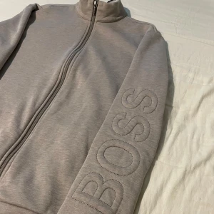 Beige/Grå stilren BOSS zip up tröja - Säljer denna helt nya stilrena BOSS zip tröjan pågrund av att den är lite stor på mig, den är köpt på Hennings och nypris ligger på 1699kr. Mitt pris går att diskutera vid snabb och enkel affär.