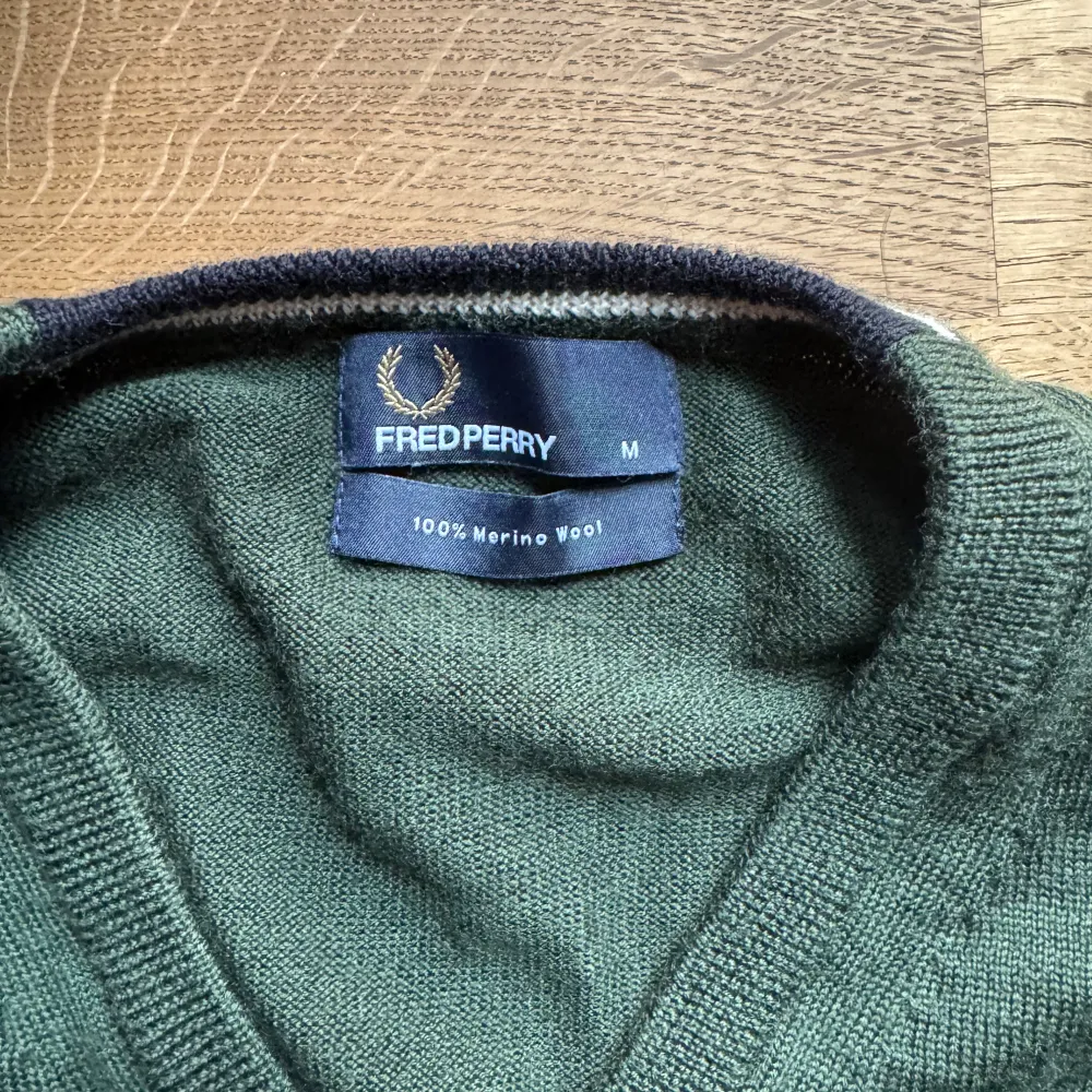 Säljer en snygg grön tröja från Fred Perry i 100% merinoull. Den har en klassisk v-ringning och långa ärmar, perfekt för höst och vinter. Tröjan är i mycket bra skick och passar både till vardags och lite finare tillfällen. Supermjuk och bekväm!. Tröjor & Koftor.