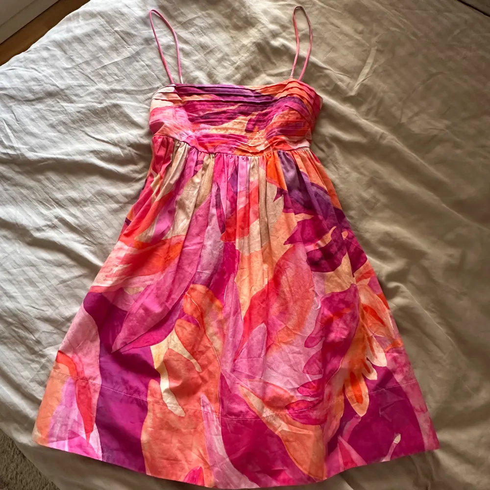 Säljer en superfin sommarklänning i härliga färger som rosa, orange och lila. Klänningen har smala axelband. Perfekt för sommarens alla fester! Den är i mycket bra skick och har en luftig passform som gör den bekväm att bära hela dagen.. Mekot.