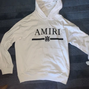 Vit hoodie från Amiri - Säljer en snygg vit hoodie från Amiri med svart logga på bröstet. Den är i bra skick och perfekt för både vardag och chill. Hoodien har en stor ficka fram och är superbekväm. Passar perfekt till jeans eller joggers!