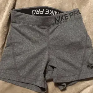 Säljer ett par grå träningsshorts från Nike Pro i mycket bra skick. De är högmidjade och har en tight passform, perfekt för gymmet eller löprundan. Materialet är stretchigt och bekvämt, vilket ger bra rörelsefrihet. Snygg och enkel design med Nike-logga på benet. Använd 2-3 gånger till vardags. xs men passar också S.