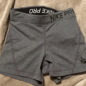 Grå träningsshorts från Nike Pro - Säljer ett par grå träningsshorts från Nike Pro i mycket bra skick. De är högmidjade och har en tight passform, perfekt för gymmet eller löprundan. Materialet är stretchigt och bekvämt, vilket ger bra rörelsefrihet. Snygg och enkel design med Nike-logga på benet. Använd 2-3 gånger till vardags. xs men passar också S.