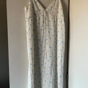 Vit blommig klänning från ADOORE - Säljer en superfin vit klänning från ADOORE med blå blommor. Den har en v-ringad design och smala axelband. Perfekt för sommarens alla fester eller en mysig dag i solen. Klänningen är i mycket bra skick och har en luftig passform.