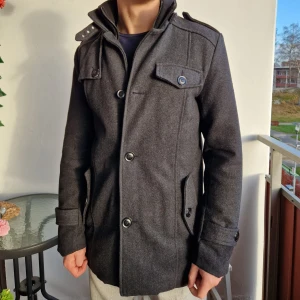 Mörkgrå rock från Indigo - Säljer en stilren varm mörkgrå rock från Indigo i mycket bra skick. Gjord i ullblandning med dubbla lager. Nypris: 1900