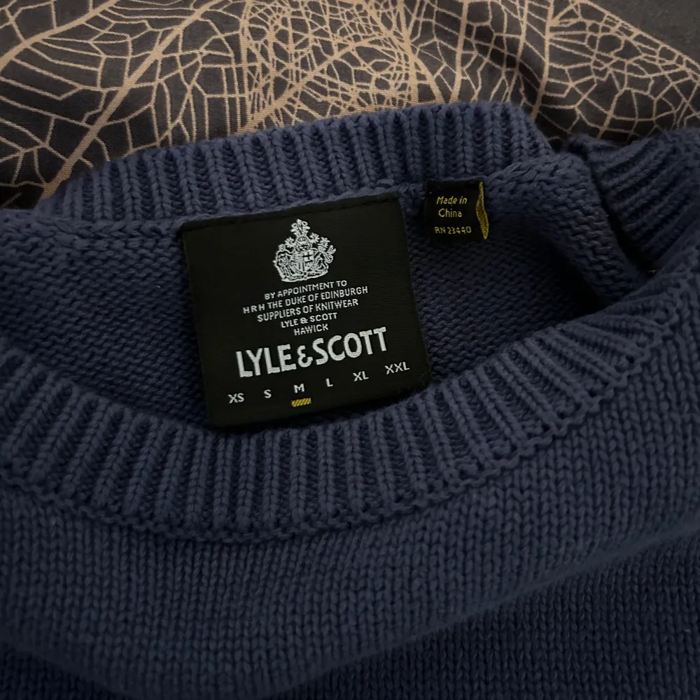 Säljer en snygg blå stickad tröja från Lyle & Scott i storlek M. Tröjan har en klassisk rund hals och ett gult broderat emblem på bröstet. Perfekt för både höst och vinter, och den är i mycket bra skick. Passar till både vardag och fest!. Tröjor & Koftor.