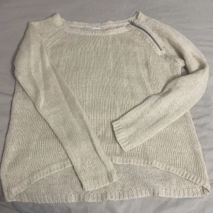 Beige stickad tröja med dragkedja - Säljer en mysig beige stickad tröja med en cool dragkedjedetalj vid halsen. Perfekt för kyliga dagar och passar både till vardags och lite finare tillfällen. Tröjan har långa ärmar och en avslappnad passform. Superfin att matcha med jeans eller kjol!
