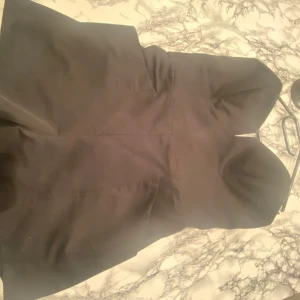 Svart byxdress med dragkedja - Snygg svart byxdress med dragkedja i ryggen. Perfekt för festliga tillfällen. Byxdressen har en elegant och stilren design som passar till många olika tillfällen.