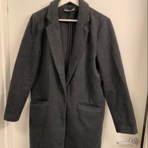 Grå kappa från Gina Tricot - Mörk grå kappa från Gina Tricot i storlek 40. Passar XS-M 90% polyester och 10% viskos, Kappan har en snygg krage och två fickor framtill.