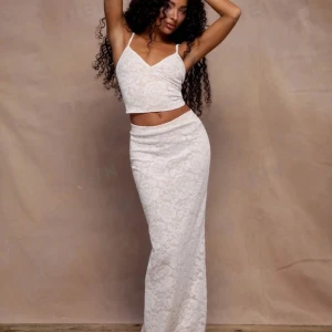 Vit spetskjol med crop top - Säljer en superfin vit spetsklänning med en matchande crop top. Klänningen är ärmlös och har en v-ringad design som ger en elegant look. Perfekt för sommarfester eller midsommarfirande. Gör den idealisk för varma dagar. Passar perfekt för dig som vill ha en stilren och chic outfit! Säljs som par