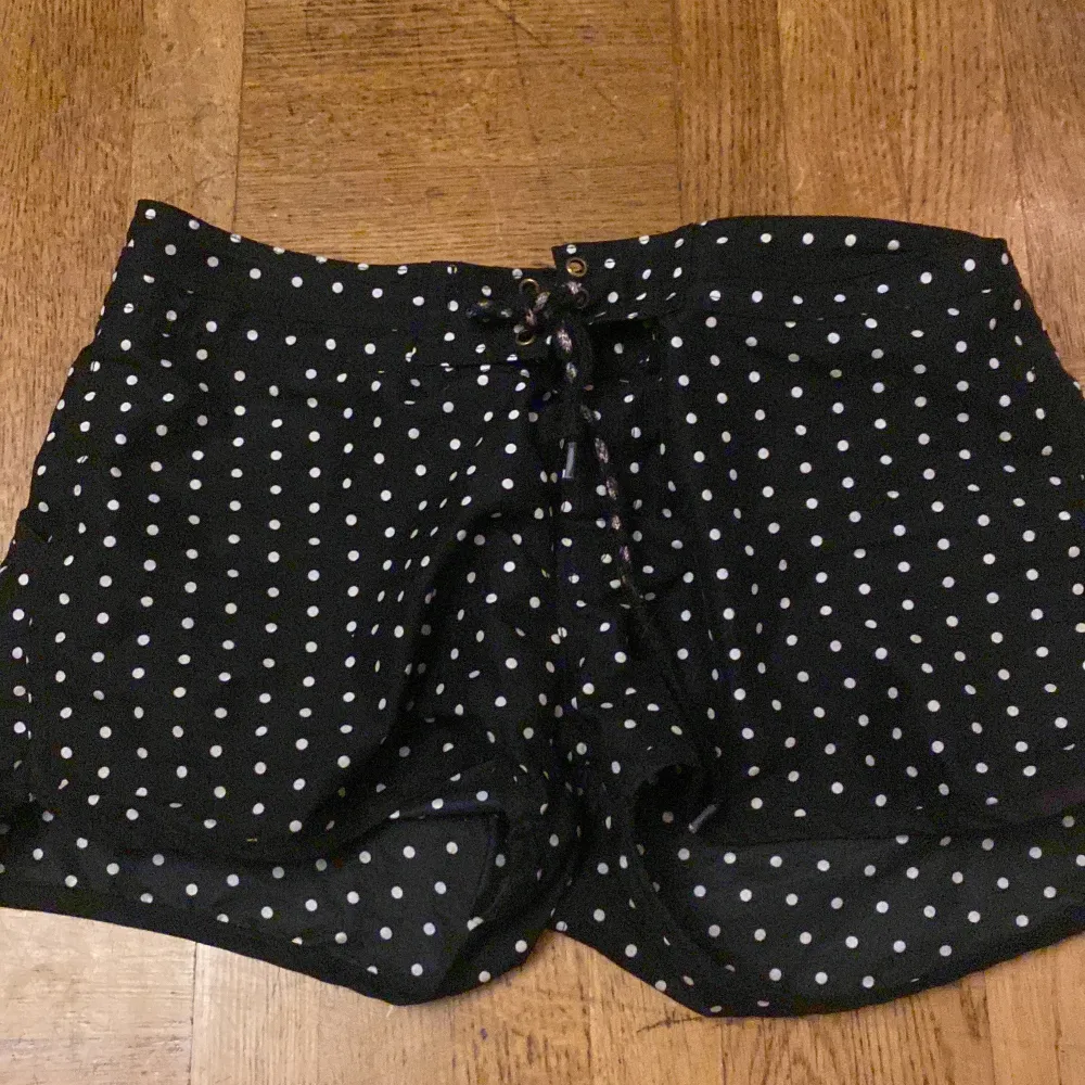 Säljer ett par svarta shorts med vita prickar. De har en bekväm passform och knytning i midjan för justerbarhet. Perfekta för sommardagar eller en avslappnad fest. Materialet känns lätt och luftigt.. Shorts.